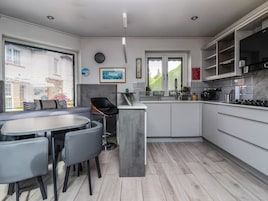 A modern kitchen with a dining area, featuring a central island, grey cabinetry, and a view of the outdoors.