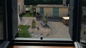 A view through an open door of a courtyard with a building, a small tree, and a paved area.