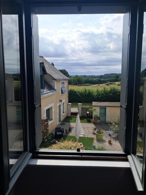 Vista desde una ventana de un edificio con jardín, un camino y una pequeña construcción.