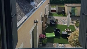 A view from a window overlooking a courtyard with a lawn, outdoor furniture, and a building with a sloped roof.