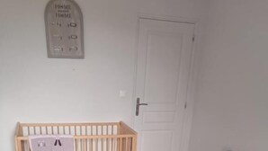 A room with a crib, a bed, a door, and a wall-mounted light switch.