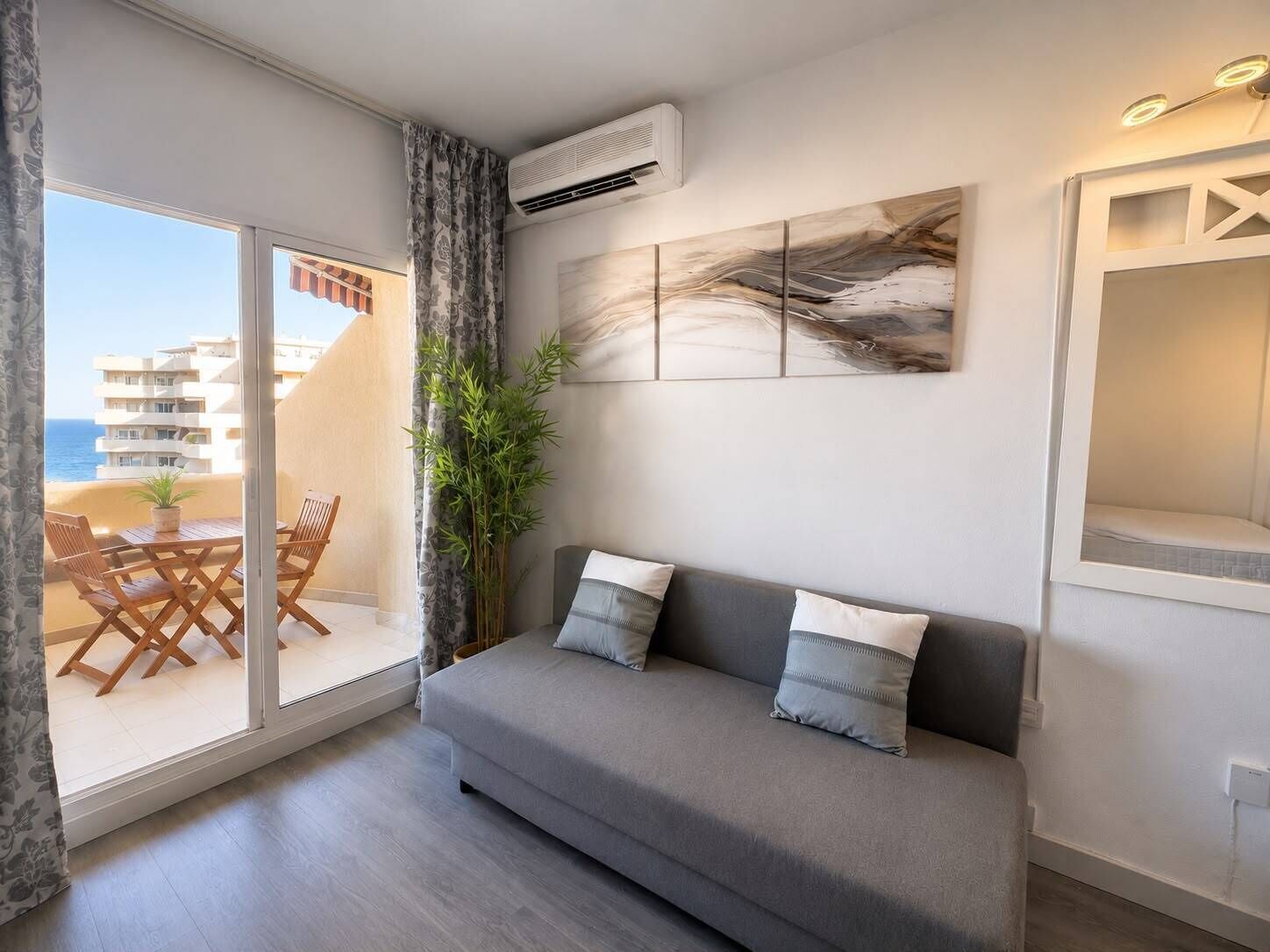 Een moderne woonkamer met een grijze bank, een groot raam met uitzicht op gebouwen, en een airconditioning.
