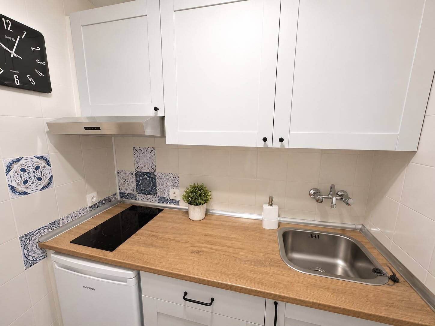 Een moderne keuken met witte kastjes, een zwarte quartz klok, een roestvrijstalen spoelbak en betegelde achterwand.