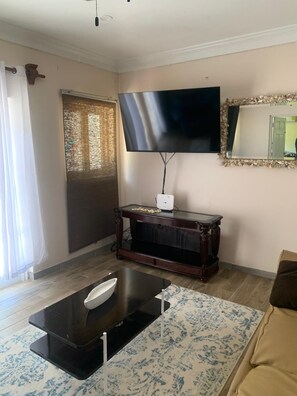 Una sala de estar con un televisor de pantalla plana montado en la pared, un mueble de madera para entretenimiento, una mesa de centro y una alfombra estampada.