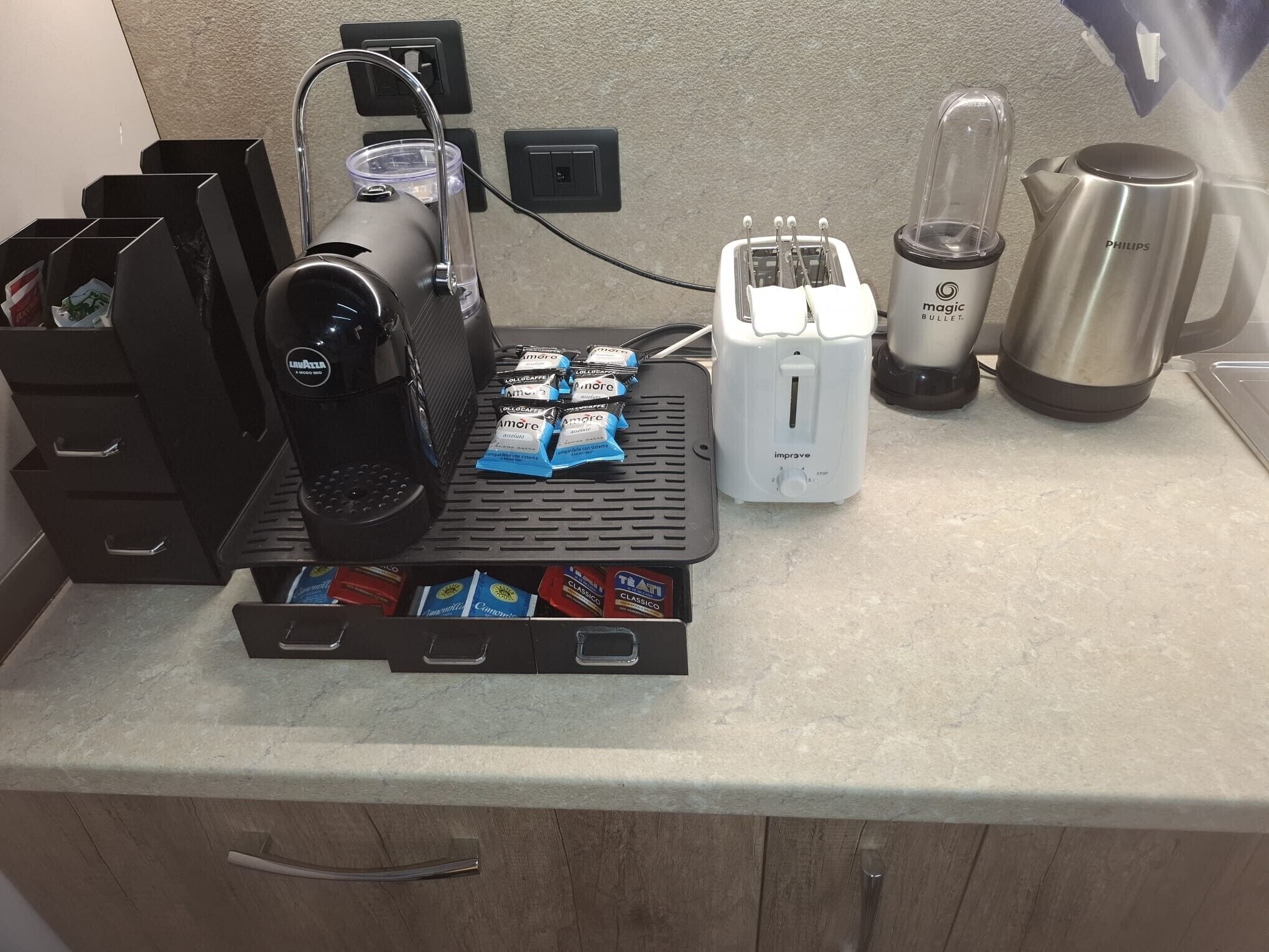 A kitchen counter with a coffee machine, toaster, blender, and coffee pods.