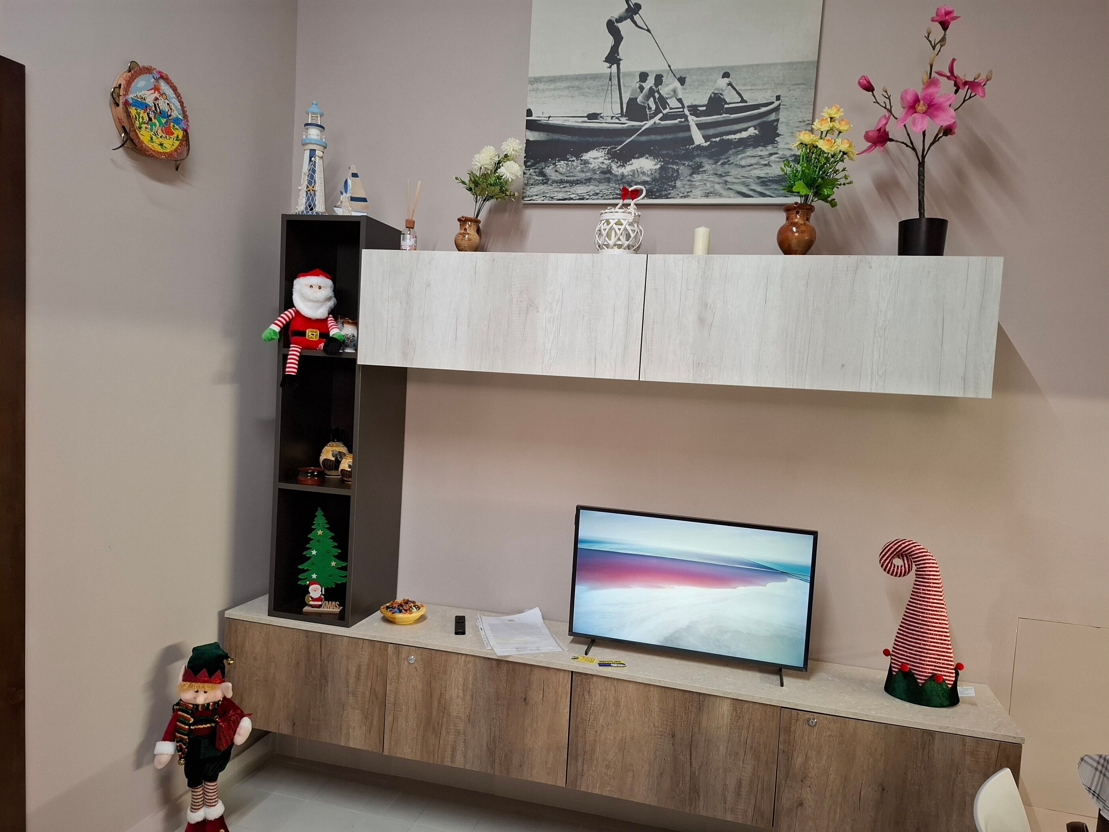Una stanza con un armadio in legno, una televisione e uno scaffale con diversi oggetti, tra cui una statuina di Babbo Natale, un albero di Natale e un quadro raffigurante una barca.