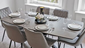 A dining table set for six with plates, cutlery, and wine glasses, surrounded by upholstered chairs. - Luxury 2-bedroom Apartment Next to Harrods (London)