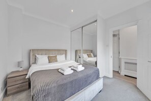 Ein modernes Schlafzimmer mit einem großen Bett, einem Nachttisch, einem Spiegel und einer Tür zu einem anderen Raum.