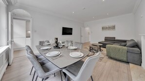 A modern dining area with a rectangular table set for four, surrounded by grey upholstered chairs. - Luxury 2-bedroom Apartment Next to Harrods (London)
