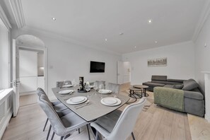 A modern dining area with a rectangular table set for four, surrounded by grey upholstered chairs.