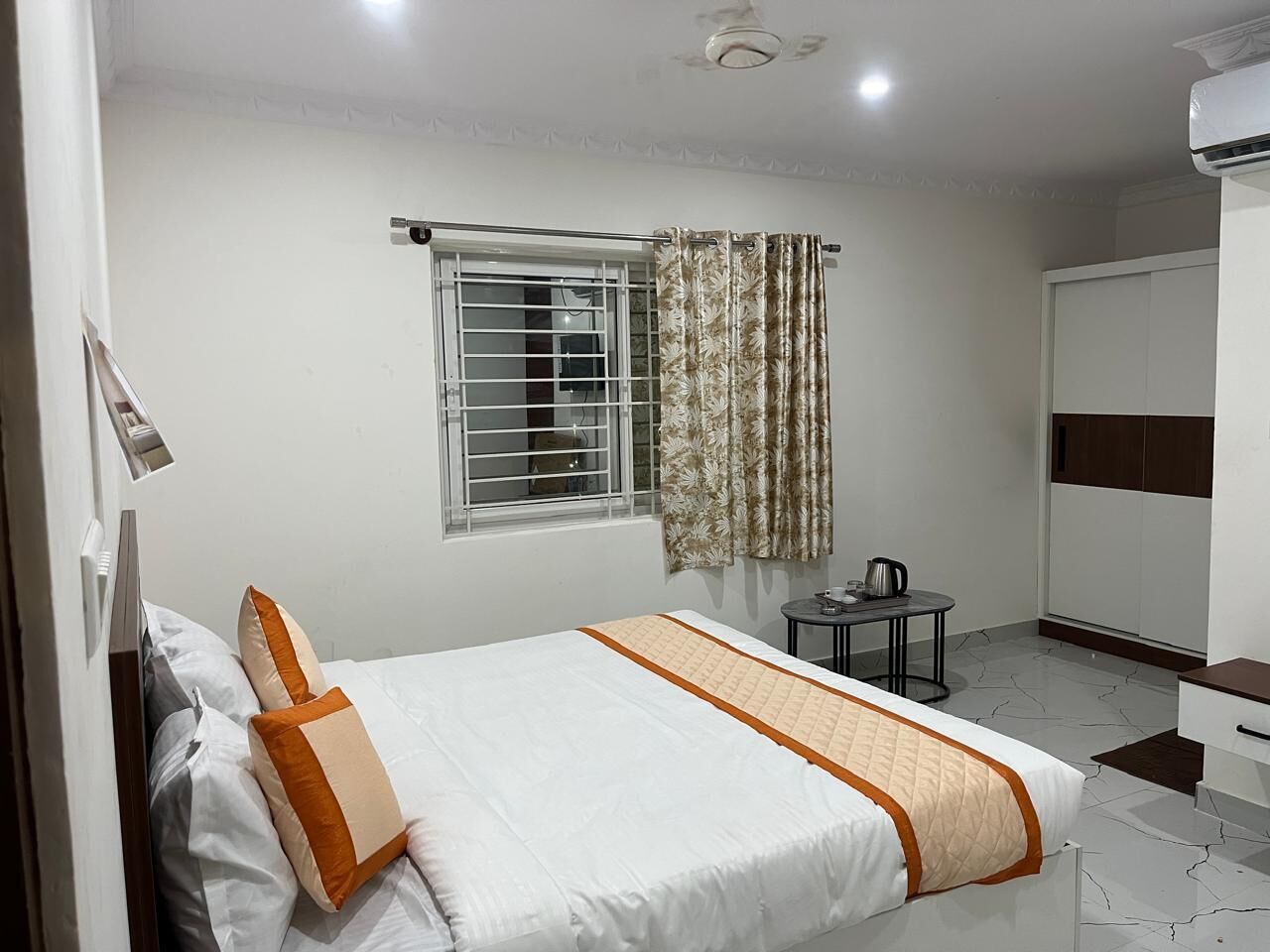 Habitación de hotel con cama, una mesita con hervidor, armario y ventana con cortinas.