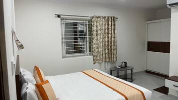 Habitación de hotel con cama, una mesita con hervidor, armario y ventana con cortinas.