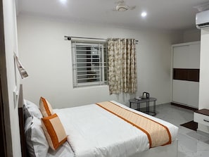 Habitación de hotel con cama, una mesita con hervidor, armario y ventana con cortinas.