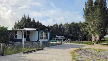 A mobile home with a fenced yard, a concrete driveway, and a forested backdrop.