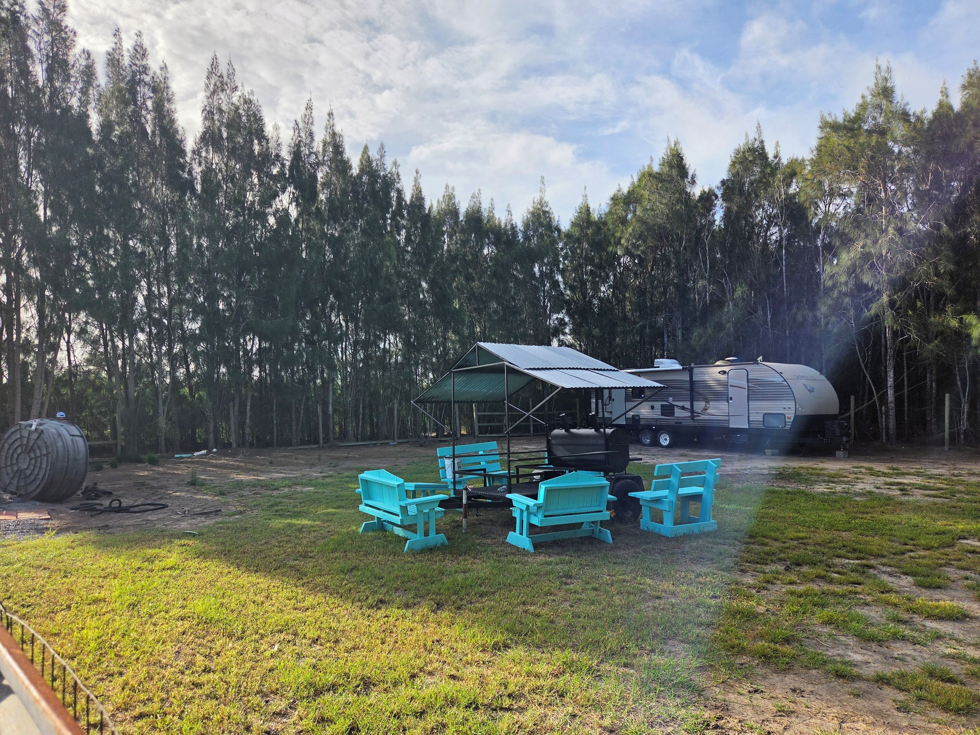 A campsite with a covered seating area, a grill, and a trailer.