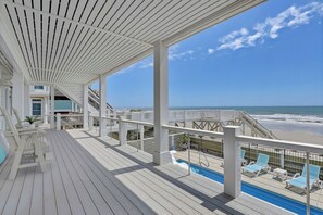 Une terrasse en bois avec une piscine, des chaises longues et une vue sur l’océan.