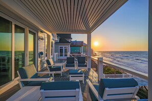 A covered outdoor seating area with chairs and tables, overlooking the ocean at sunset. - On Porpoise #223 | Luxury Oceanfront Escape in North Topsail Beach (North Topsail Beach)