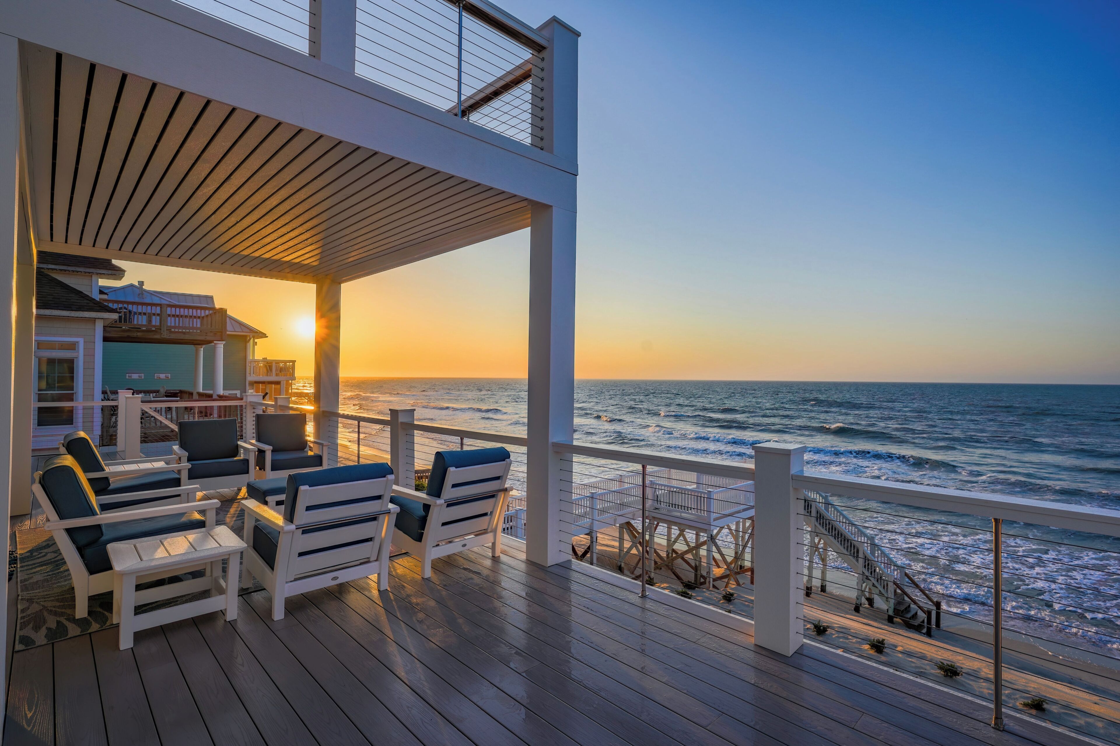 A deck with outdoor seating overlooking the ocean at sunset.