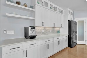 A modern kitchen with white cabinetry, a black refrigerator, and a coffee machine. - On Porpoise #223 | Luxury Oceanfront Escape in North Topsail Beach (North Topsail Beach)