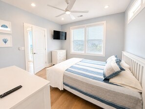 Une chambre à coucher avec un lit, une télévision, un bureau et un ventilateur de plafond.