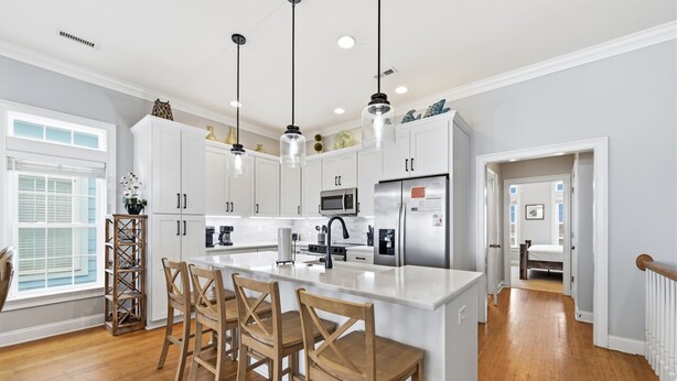 A modern kitchen with white cabinets, a central island with bar stools, pendant lighting, and a view into the adjacent bedroom. - Beach Walk #225-Oceanfront Duplex in Surf City, Pool, Elevator, Dog Friendly! (Surf City)