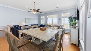 A dining area with a wooden table and chairs, a ceiling fan, and a large window with a view. - Beach Walk #225-Oceanfront Duplex in Surf City, Pool, Elevator, Dog Friendly! (Surf City)