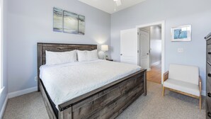 A bedroom with a bed, a ceiling fan, a nightstand, a chair, and artwork on the walls. - Beach Walk #225-Oceanfront Duplex in Surf City, Pool, Elevator, Dog Friendly! (Surf City)