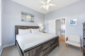 Ein Schlafzimmer mit einem Bett, einem Deckenventilator, einem Nachttisch, einem Sessel und Kunstwerken an den Wänden.