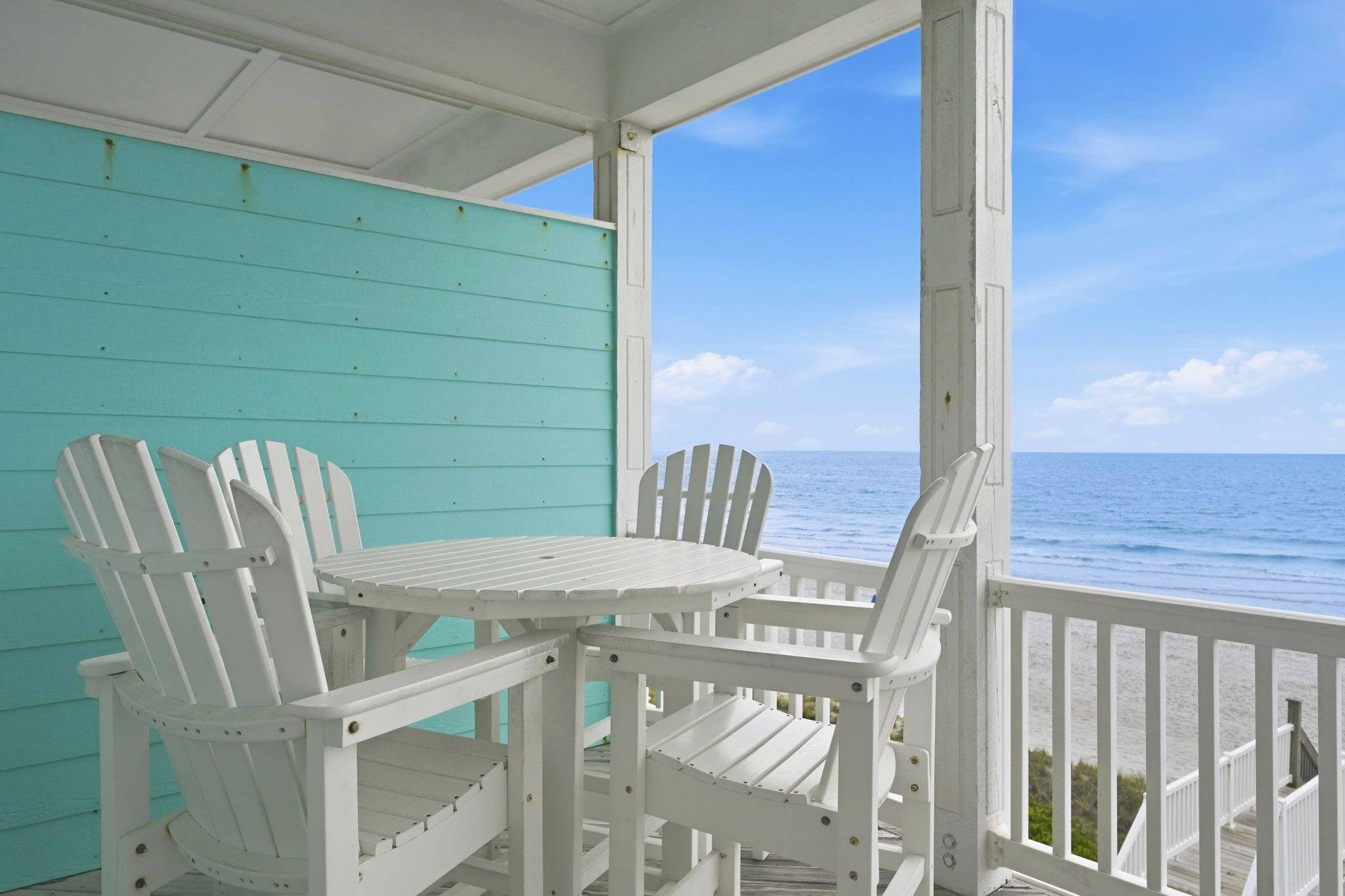A covered outdoor seating area with a table and two Adirondack chairs, overlooking a body of water.