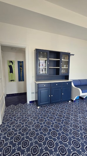 Ein Zimmer mit dunkelblauem Teppichmuster, einem dunkelblauen Schrank mit Glastüren und einer weißen Wand mit zwei abstrakten Gemälden.