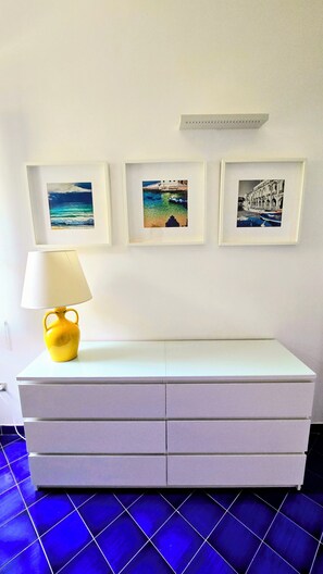 Ein weißer Kommode mit Schubladen, eine gelbe Lampe und drei gerahmte Bilder an der Wand.