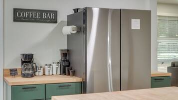 Uma cozinha com geladeira de aço inoxidável, cafeteira e um letreiro que diz 'Coffee Bar love is brewing'.