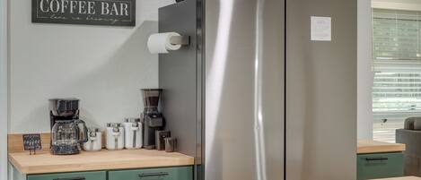 A kitchen with a stainless steel refrigerator, a coffee maker, and a sign that reads 'Coffee Bar love is brewing.'