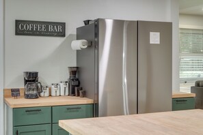 Uma cozinha com geladeira de aço inoxidável, cafeteira e um letreiro que diz 'Coffee Bar love is brewing'.