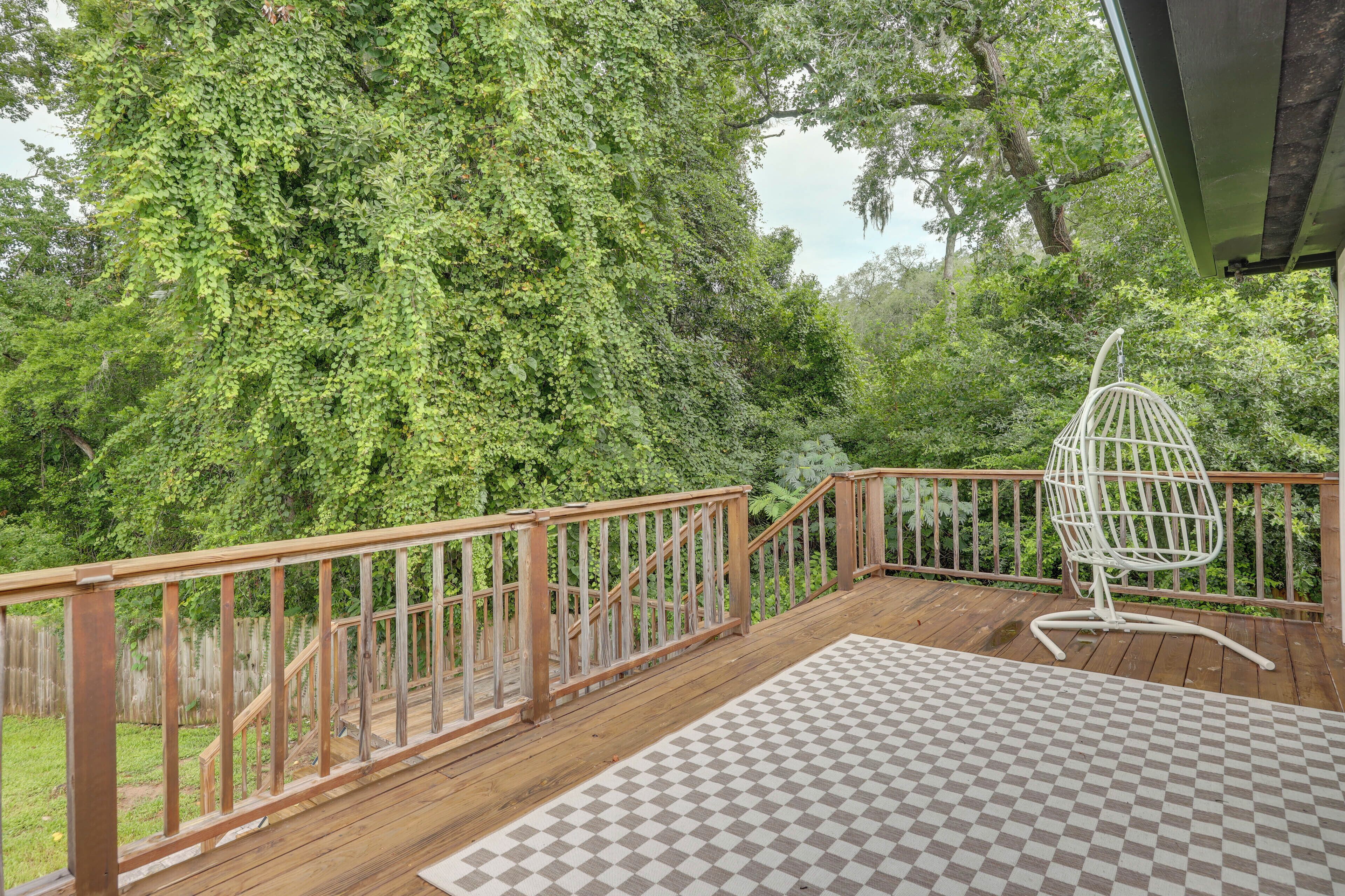 A wooden deck with a checkered mat, a white hanging chair, and a view of dense greenery.