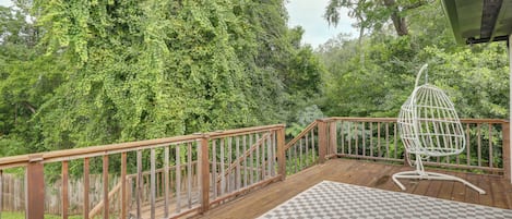 A wooden deck with a checkered mat, a white hanging chair, and a view of dense greenery.