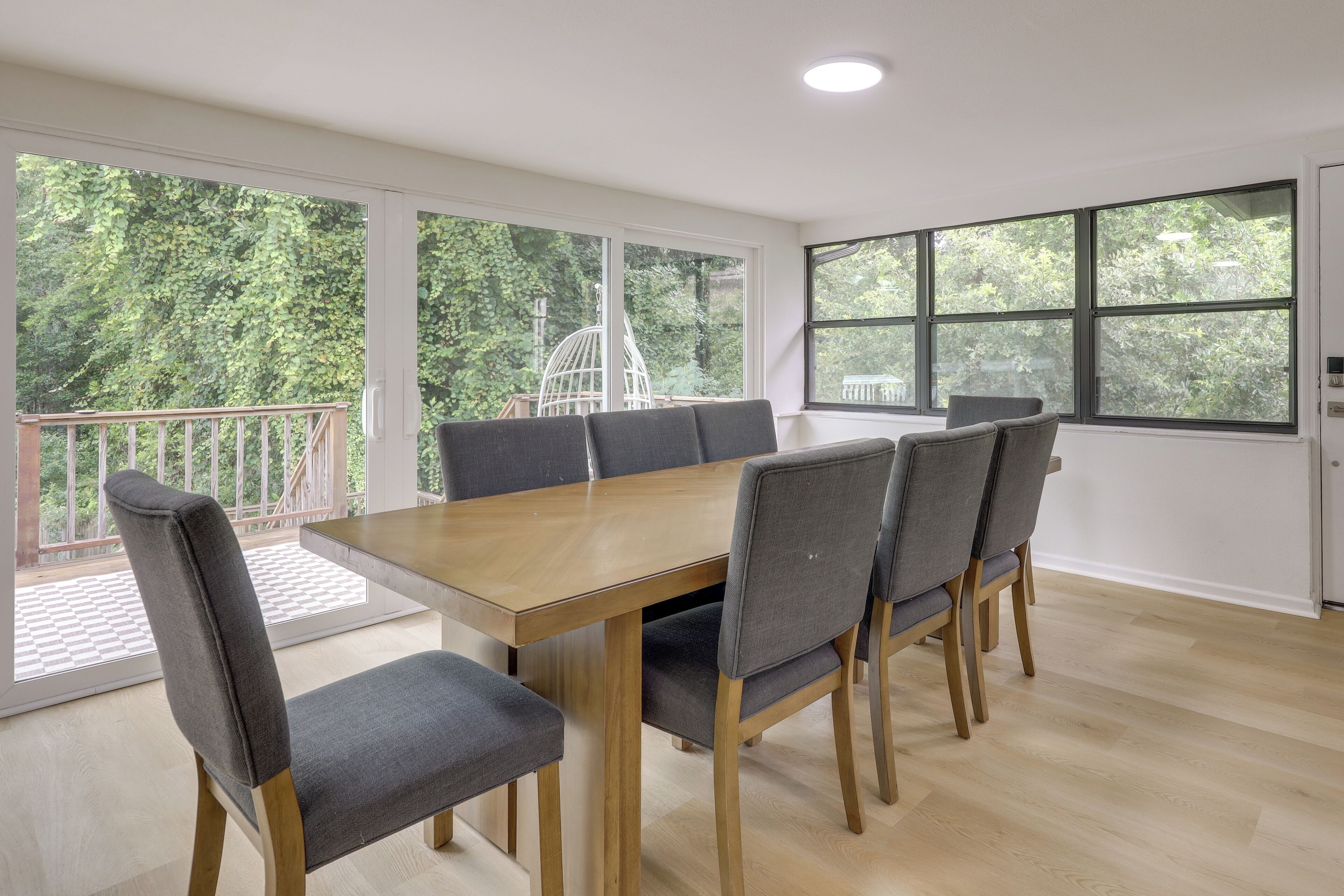 Uma sala de conferências com uma mesa de madeira e cadeiras estofadas cinzentas, grandes janelas com vista para áreas verdes e um teto branco com iluminação embutida.