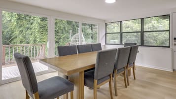 Uma sala de conferências com uma mesa de madeira e cadeiras estofadas cinzentas, grandes janelas com vista para áreas verdes e um teto branco com iluminação embutida.