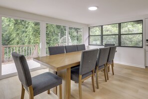 Ein Konferenzraum mit einem Holztisch und grau gepolsterten Stühlen, großen Fenstern mit Blick auf Grünflächen und einer weißen Decke mit eingelassenen Leuchten.