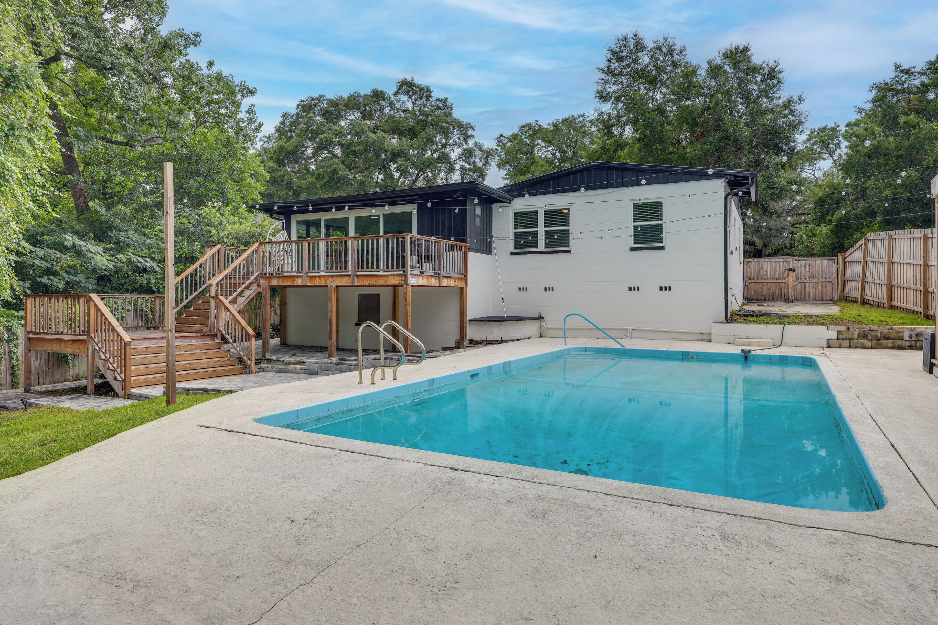 Uma casa com piscina, deck de madeira e quintal cercado.