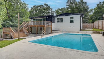 Uma casa com piscina, deck de madeira e quintal cercado.