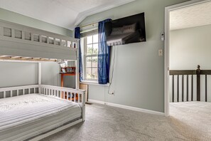 A room with a bunk bed, a crib, a window with curtains, a wall-mounted TV, and a door leading to another room. - 1 Mi to Eagle Creek Res: Family-friendly Indy Home (Indianapolis)