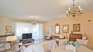 Habitación de hotel con televisor, zona de estar, candelabro y obras de arte.