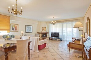 A well-lit living room with a fireplace, a television, and a dining area with a table set for two. - Ellinikon Sea View (Argiroupoli)