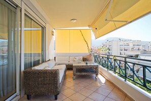 A balcony with a sofa, two side tables, a potted plant, and a view of buildings. - Ellinikon Sea View (Argiroupoli)