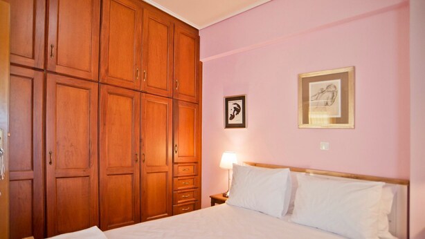 Habitación de hotel con un amplio armario de madera, una cama con ropa blanca y dos cuadros en la pared.