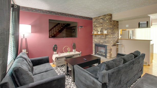 A living room with a fireplace, a television mounted on the wall, and a staircase leading to another level. - 5 Mi to Downtown Davenport! Townhome w/ Patio (Davenport)