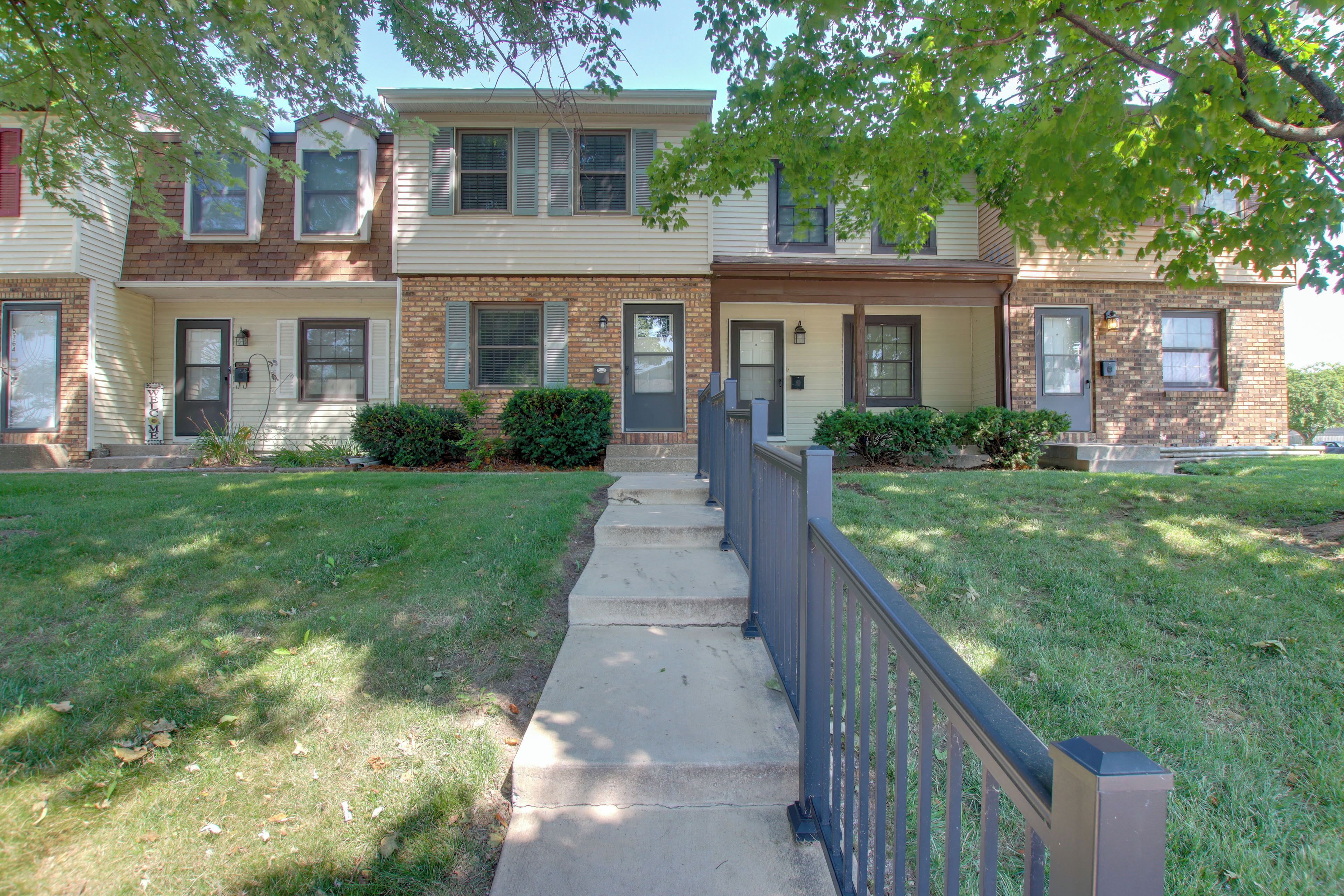 A two-story residential building with a front entrance, a small front yard, and a sidewalk leading to the door.
