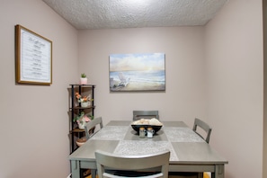 A dining area with a table set for four, a framed menu on the wall, a painting of a beach scene, and a small plant on a shelf. - 5 Mi to Downtown Davenport! Townhome w/ Patio (Davenport)