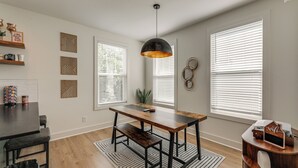 Comedor con una mesa de madera, sillas de metal negro, una lámpara colgante negra y un tapete estampado.